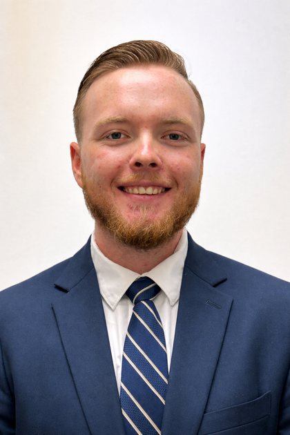 Logan Cope, smiling, in a navy suit and striped tie